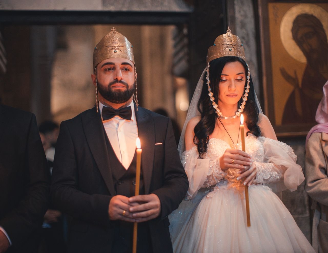A bride and groom holding candles during a traditional wedding ceremony indoors.
